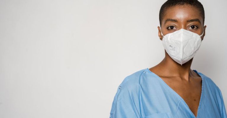 Wall Safe - Serious African American female doctor in medical mask and blue uniform standing against white background