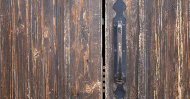 Safe Lock - Closeup of weathered old rusty brown locked wooden door with cracks on surface with aged metal handle