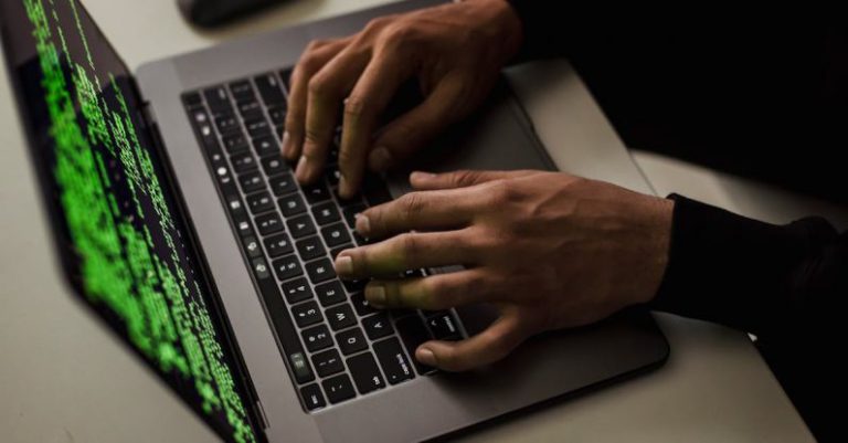 Access Control - From above of crop anonymous male hacker typing on netbook with data on screen while sitting at desk