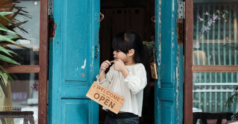 Door - Photo of Girl Holding Wooden Welcome Signage While Standing on Doorway