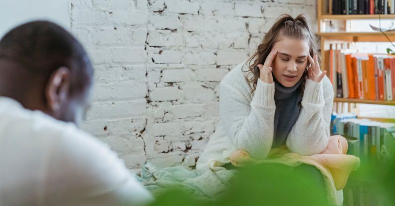 Lockout Situations - Exhausted woman calming down after argument with husband by putting fingers on temples and man sitting and looking down