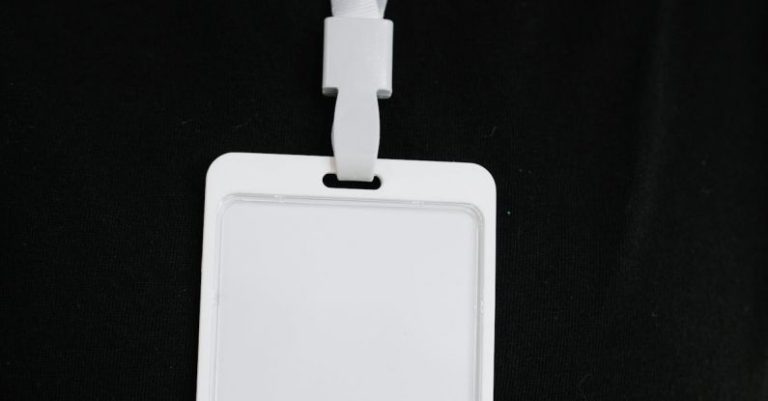 Security Upgrades - Plastic name tag with white ribbon and blank paper hanging on black background