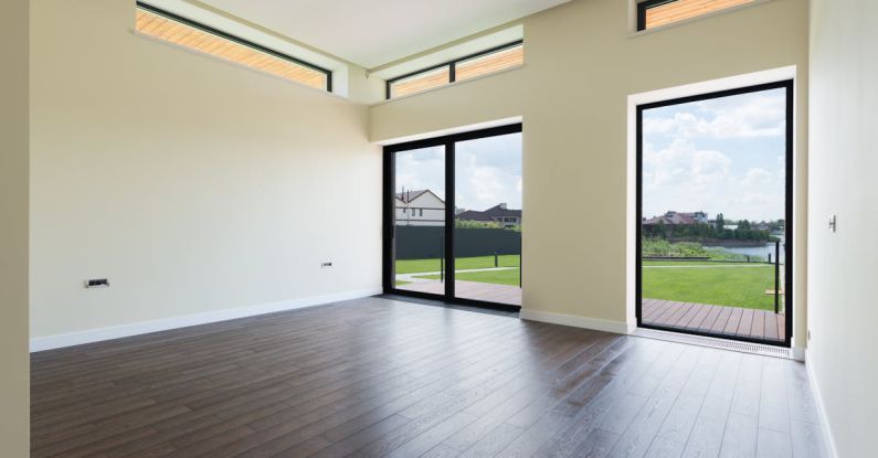 Keyless Entry - Interior of spacious room with wooden laminate floor big windows and glass door viewing terrace and green lawn